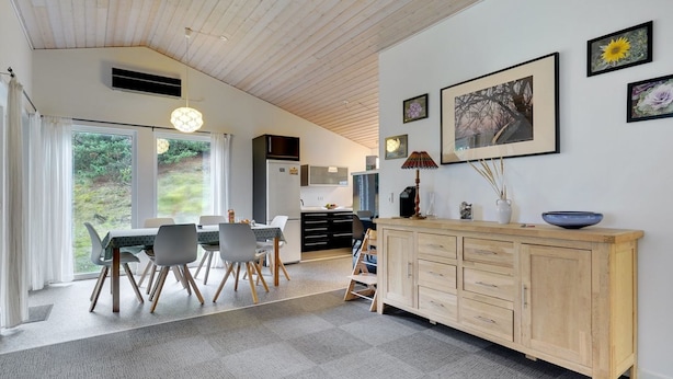 A modern kitchen with a wooden cabinet, a dining area with a table and chairs, and a large window with a view of greenery.