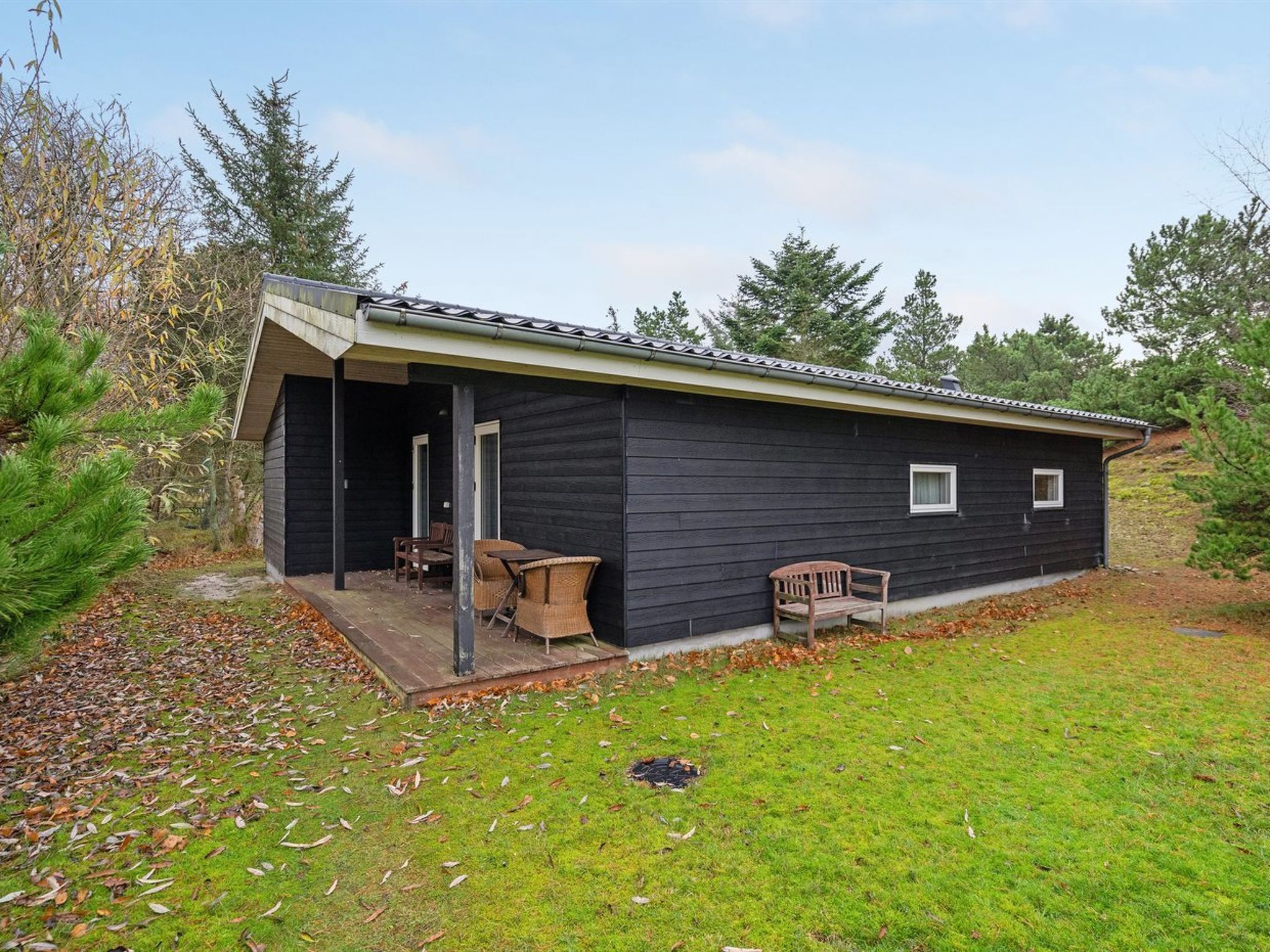 A small, single-story cabin with a porch and two wicker chairs.