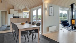 Eine moderne Küche mit Holzschränken, ein Essbereich mit einem weißen Tisch und schwarzen Stühlen sowie ein großes Fenster mit Blick ins Freie.