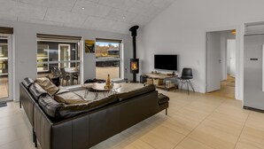 A spacious living room with a large black sofa, a fireplace, a flat-screen TV, and a dining area with a table and chairs. - "Tatiane" - 1.5km from the sea by Interhome (Løkken)