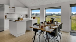A modern kitchen with white cabinetry, a central island, and a dining area with a wooden table and chairs. - "Tatiane" - 1.5km from the sea by Interhome (Løkken)