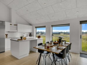 Une cuisine moderne avec des meubles blancs, un îlot central et un coin repas comprenant une table et des chaises en bois.