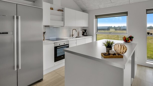 A modern kitchen with a Bosch refrigerator, white cabinetry, a built-in oven, and a large window overlooking a field. - "Tatiane" - 1.5km from the sea by Interhome (Løkken)