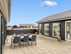 Une terrasse avec une table et des chaises, une grande fenêtre et une vue sur d’autres immeubles.