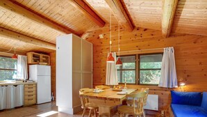 A cozy cabin with a wooden interior, a dining area with a table and chairs, a kitchenette, and a blue sofa.
