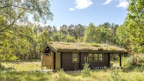A rustic cabin with a thatched roof, surrounded by dense forest.