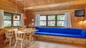 A wooden cabin with a dining area, a blue sofa, and a television.