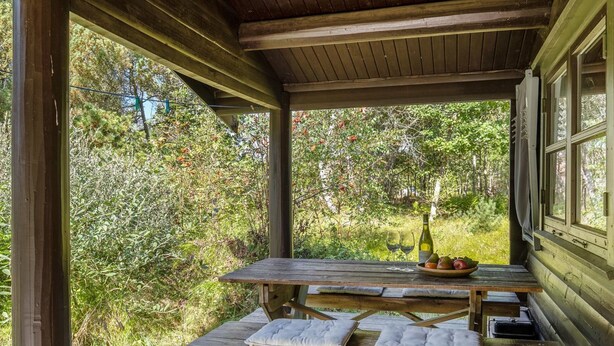 A wooden deck with picnic tables, a bottle of wine, and a bowl of fruit.