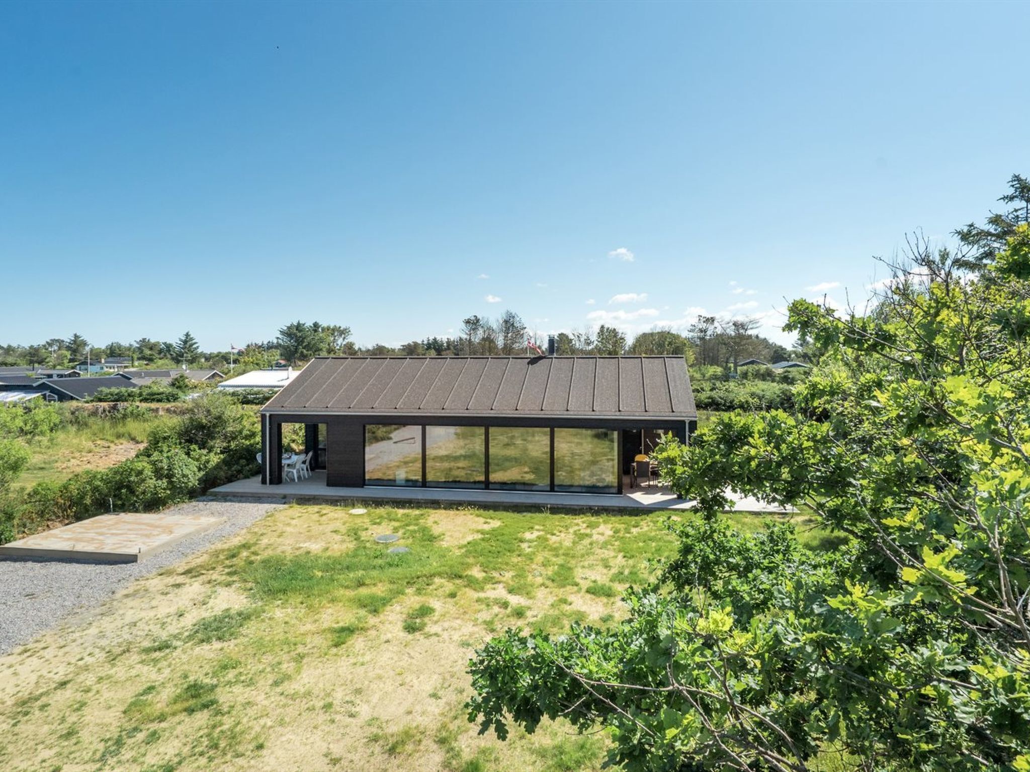 Una casa moderna con un'ampia facciata in vetro, immersa nel verde sotto un cielo sereno.