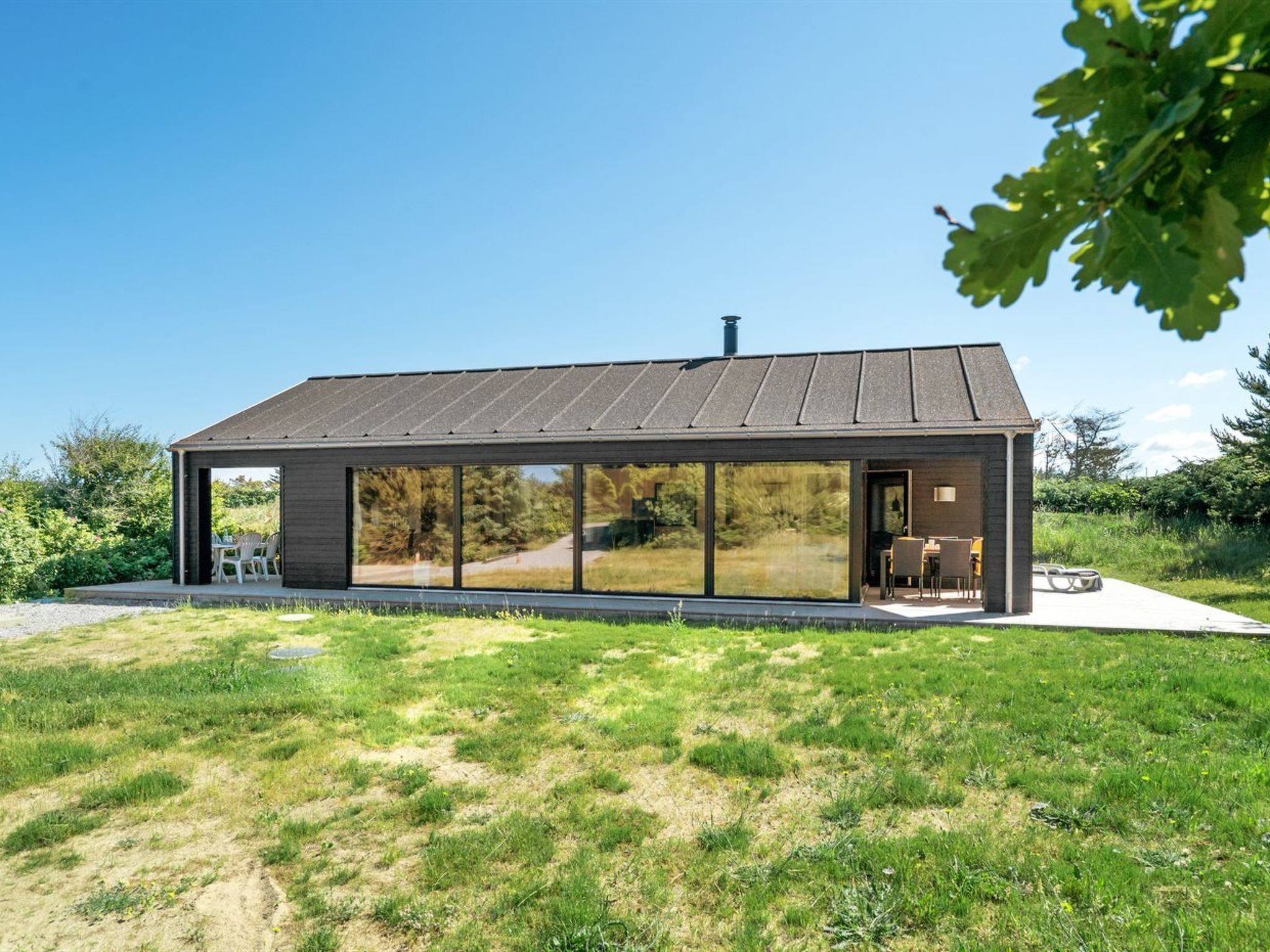 Une maison moderne dotée de grandes fenêtres en verre, d’un toit plat et d’un petit espace extérieur aménagé pour s’asseoir.