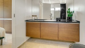 A modern bathroom with a large mirror, wooden cabinets, a black countertop, and a potted plant.