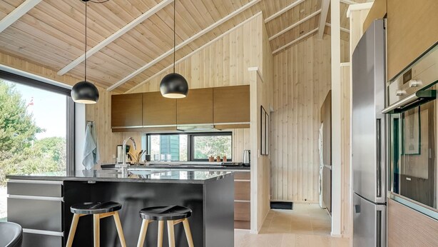 A modern kitchen with a large island, wooden accents, stainless steel appliances, and a view of greenery outside.