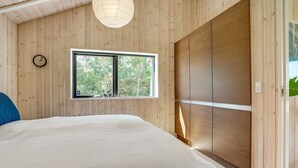 A bedroom with a large bed, a window with a view of trees, a wooden wardrobe, and a clock on the wall.