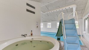 En stor indendørs swimmingpool med rutsjebane, jacuzzi og et vindue med naturligt lys.