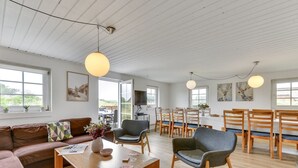 En rummelig stue med trægulv, en brun lædersofa, en grå lænestol og et træspisebord med seks stole.