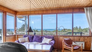 A room with a wooden ceiling, large windows with a view of the beach, a purple sofa, a wooden table, and a leather chair. - "Frender" - 150m from the sea by Interhome (Læsø)