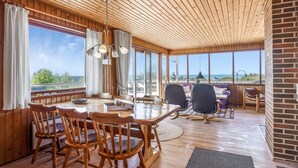A wooden dining area with a large table and chairs, large windows with a view of the ocean, and a brick wall on the right. - "Frender" - 150m from the sea by Interhome (Læsø)