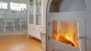 A room with a wood-burning stove, a dining area with chairs, and a window with a view.