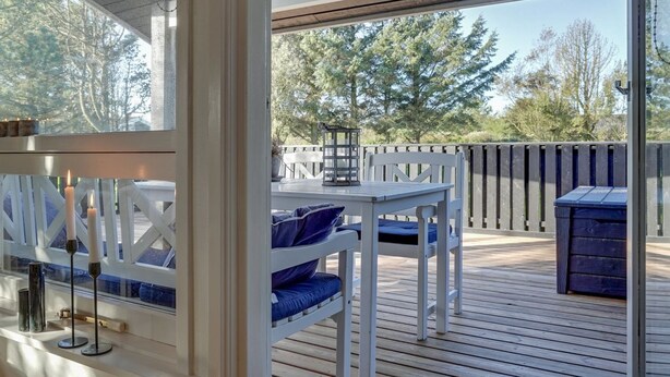 A covered outdoor deck with a table and chairs, a lantern, and a trash bin.