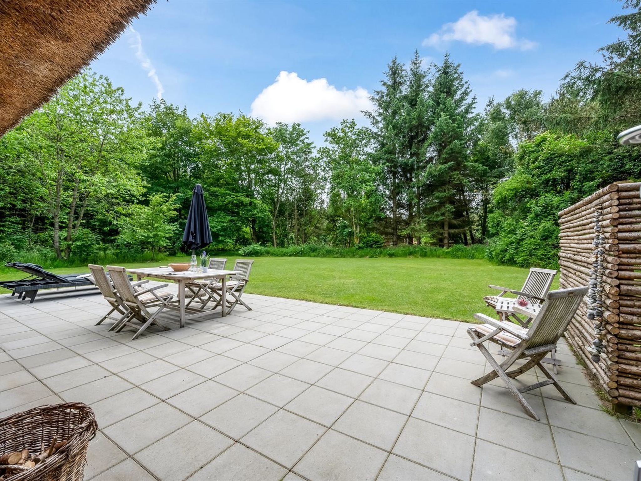 Un espace patio aménagé avec une table et des chaises, entouré d’une pelouse verdoyante et luxuriante ainsi que d’arbres.