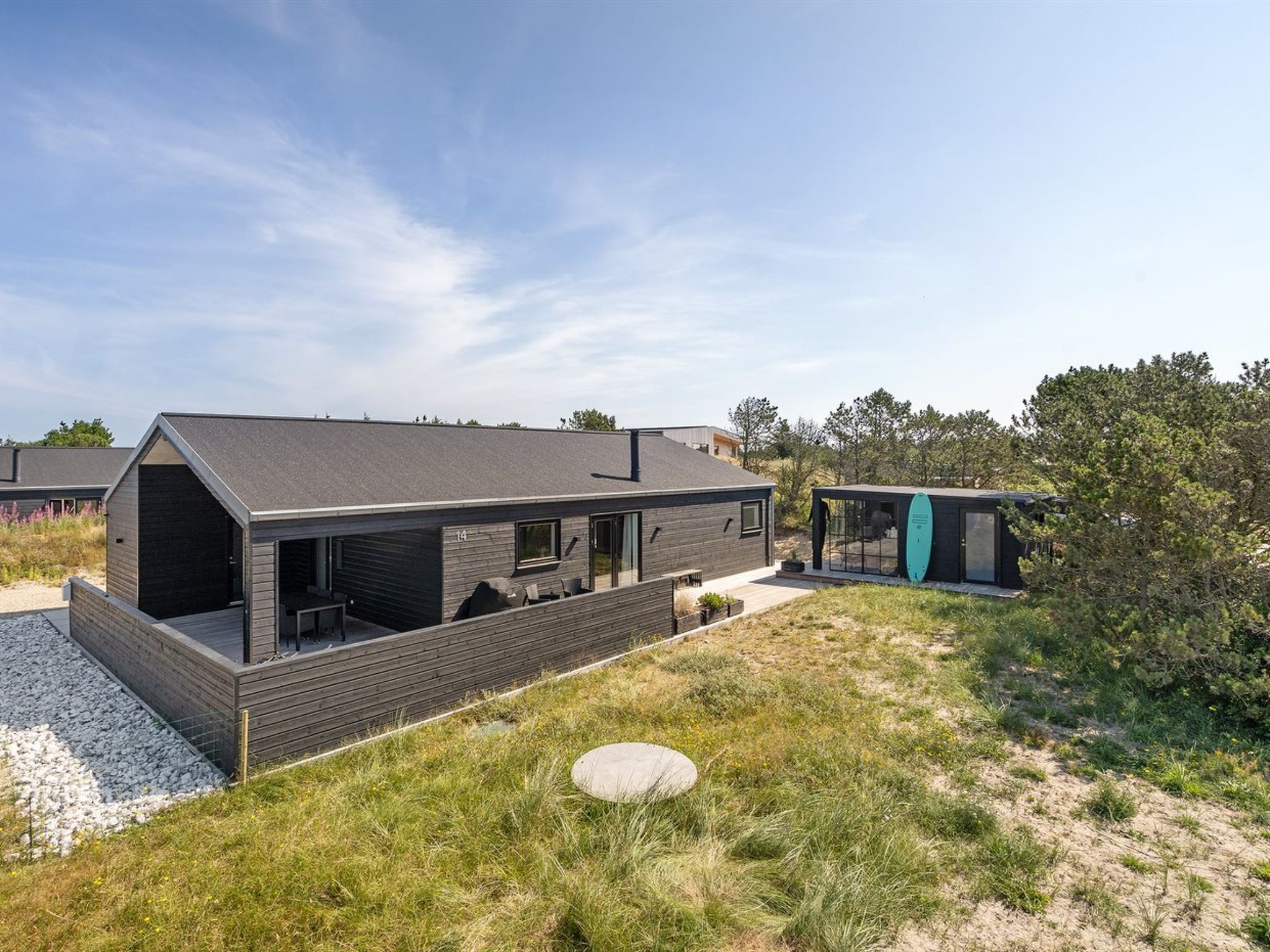 Une maison moderne dotée d’une grande terrasse et d’une structure séparée en verre.