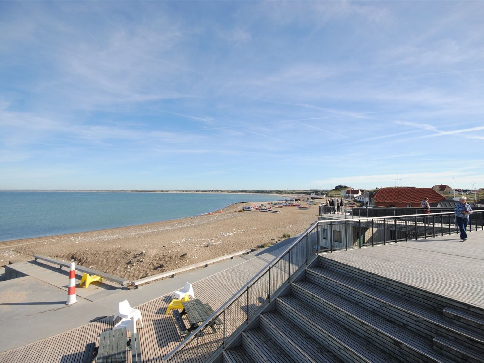 Une plage avec une promenade en bois, des chaises de plage et des parasols.