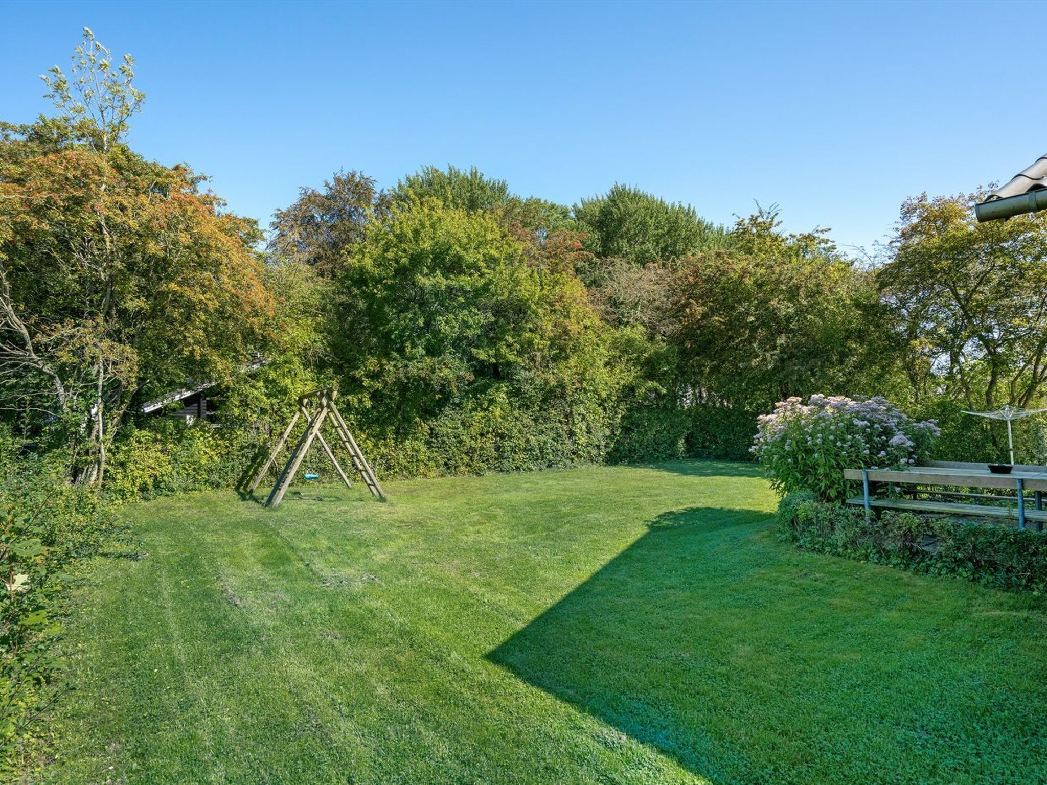A well-maintained lawn with a wooden swing set and a picnic table in a serene garden setting.