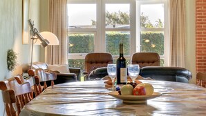Un coin repas avec une table ronde, des chaises, une bouteille de vin et un saladier de fruits.