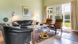 Un salon avec un canapé en cuir noir, une table basse ronde, deux fauteuils en cuir, un lampadaire et un tableau accroché au mur.
