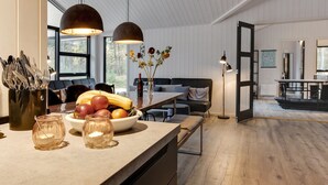 A modern kitchen with a wooden countertop, a bowl of fruit, and a vase with flowers. There is a dining area with a table and chairs, and a sofa in the background. - "Eliz" - 800m from the sea by Interhome (Nexø)