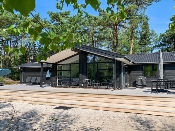 Ein modernes Gebäude mit überdachter Terrasse, Sitzgelegenheiten im Freien und einer Grillvorrichtung.