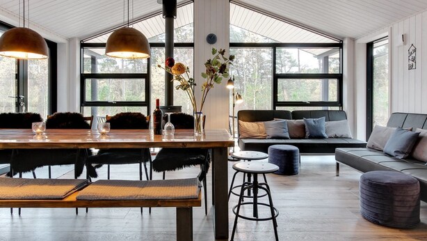 A spacious living area with a wooden dining table, black chairs, a black sofa, and a large window offering a view of trees. - "Eliz" - 800m from the sea by Interhome (Nexø)