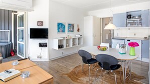 A modern kitchen with white cabinets, a dining area with a wooden table and black chairs, and a TV mounted on the wall.
