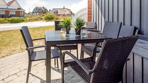 An outdoor patio with a table and chairs, potted plants, and a view of houses in the background.