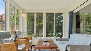 A sunlit room with wicker furniture, a wooden table, and large windows offering views of trees and a fence. - "Ømund" - 600m to the fjord by Interhome (Holbæk)