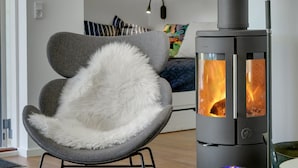 A modern living room with a grey armchair, a round table with two blue candles, and a wood-burning stove. - "Rikkie" - 150m to the fjord by Interhome (Rørvig)