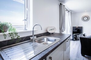 A modern kitchen with a stainless steel sink, a window with a view, and a flat-screen TV. - Beach View - 2 Bed Apartment - Llanelli (Llanelli)