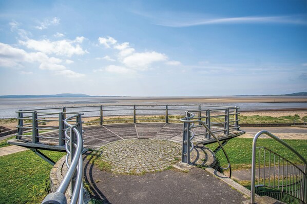 A circular viewing platform with metal railings, a paved area with a cobblestone pattern, and a grassy foreground. - Beach View - 2 Bed Apartment - Llanelli (Llanelli)