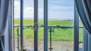 A view from a room with large windows overlooking a grassy area with a metal railing and a distant shoreline.