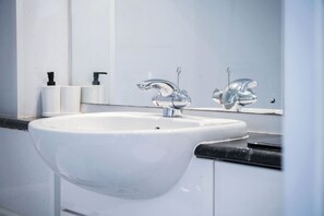 A bathroom with a white sink, chrome faucets, a mirror, and a black countertop. - Beach View - 2 Bed Apartment - Llanelli (Llanelli)