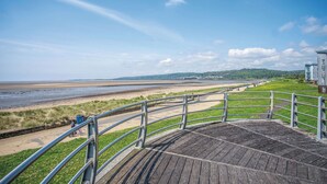 A wooden boardwalk with metal railings overlooking a beach and distant hills.