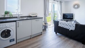 A modern kitchen with a built-in washer, a dining area with a black sofa, and a TV.