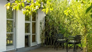 Un edificio con amplios ventanales y un patio empedrado con dos sillas.