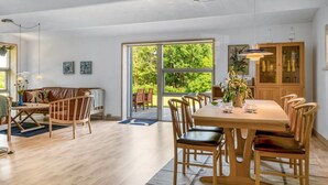 Un comedor espacioso con una gran mesa y sillas, un aparador de madera y vistas a la vegetación a través de puertas correderas.
