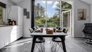 A modern kitchen with a dining area, large windows, and a view of the outdoors.