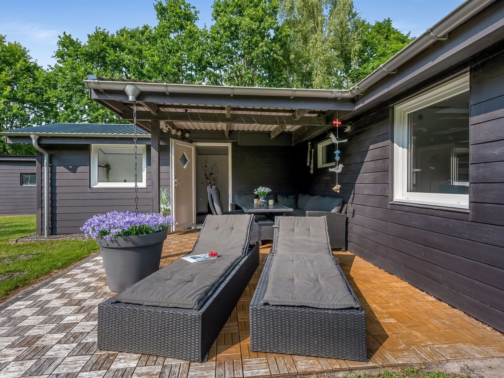 A covered outdoor seating area with two lounge chairs and a table, surrounded by a wooden deck.