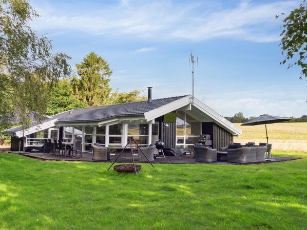 A modern house with a covered patio, outdoor seating, and a large window overlooking a grassy field.