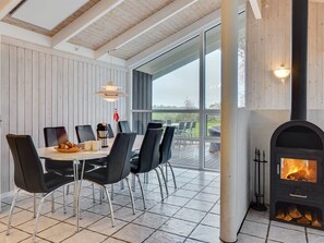 A modern dining area with a large table, black chairs, and a wood-burning stove.