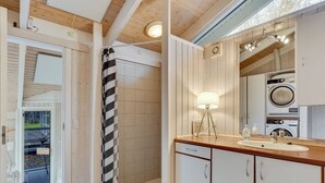 A bathroom with a shower, a sink, a mirror, and a washing machine.