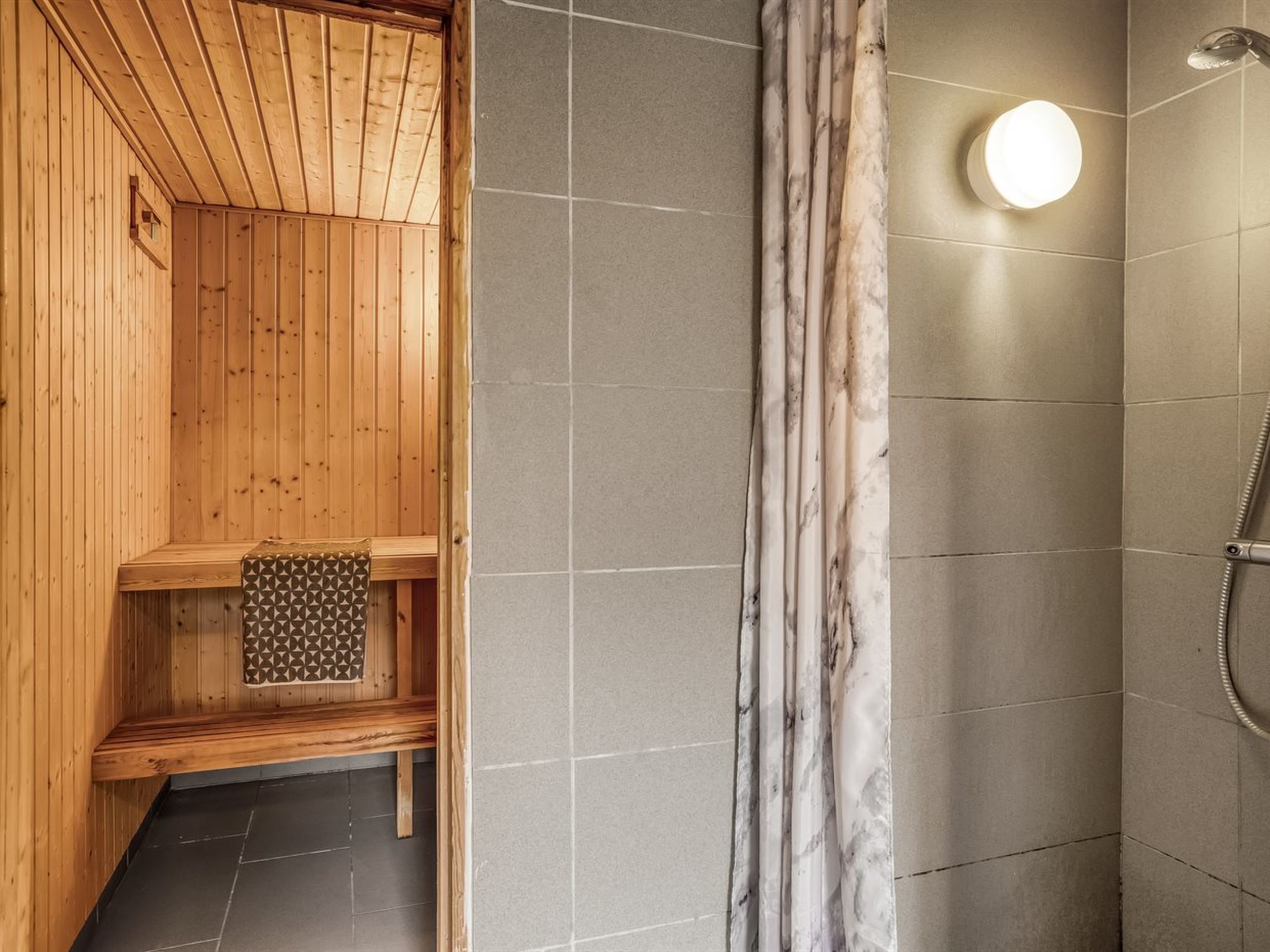 En sauna med trævægge og flisegulv, en bænk med et håndklæde og et bruseområde med en marmorforhæng.